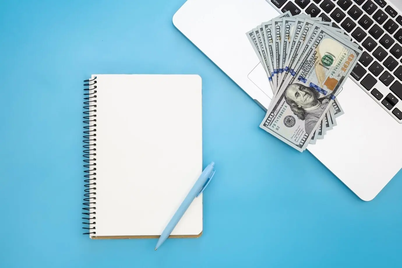 Draufsicht: Leerer Notizblock und Geld auf einem Laptop.